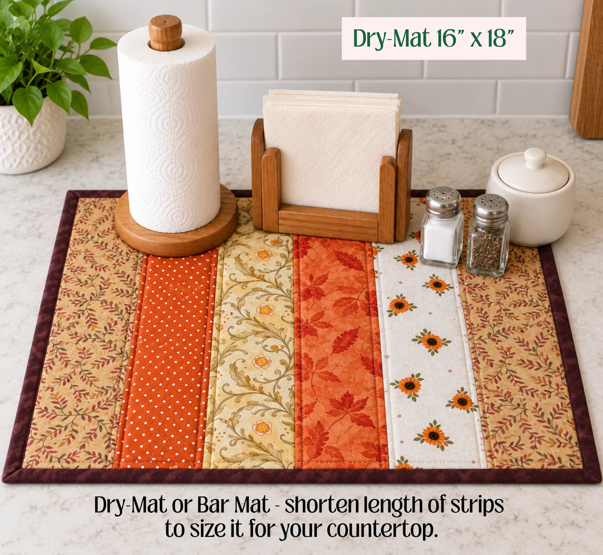 A quilted bar mat with vertical fabric strips in orange, beige, and floral patterns, displayed on a kitchen countertop with paper towels, napkins, and condiments. Text overlays indicate the size as 16" x 18" and explain that the mat can be shortened to size for countertop use.
