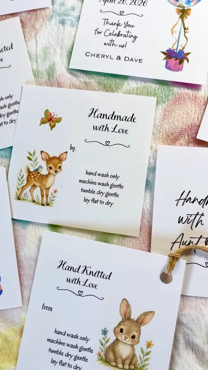 A styled flat-lay of personalized baby gift tags and matching cards on a pastel patterned fabric background. The white paper tags feature cute illustrations (woodland animals) of a deer, a rabbit, and a butterfly, for baby showers, and baby gifts.